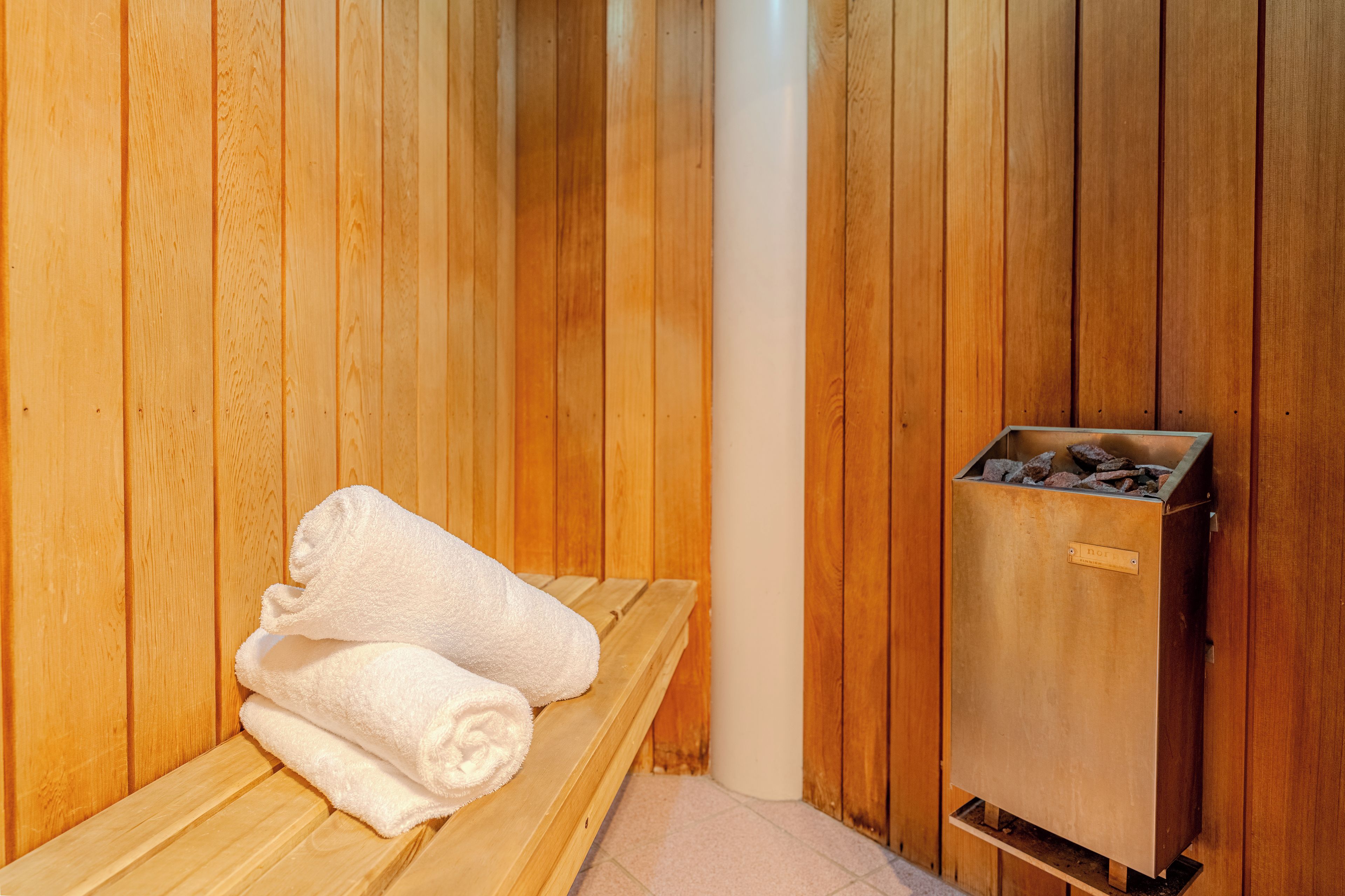 A sauna room with wooden walls, a bench, and a sauna heater.