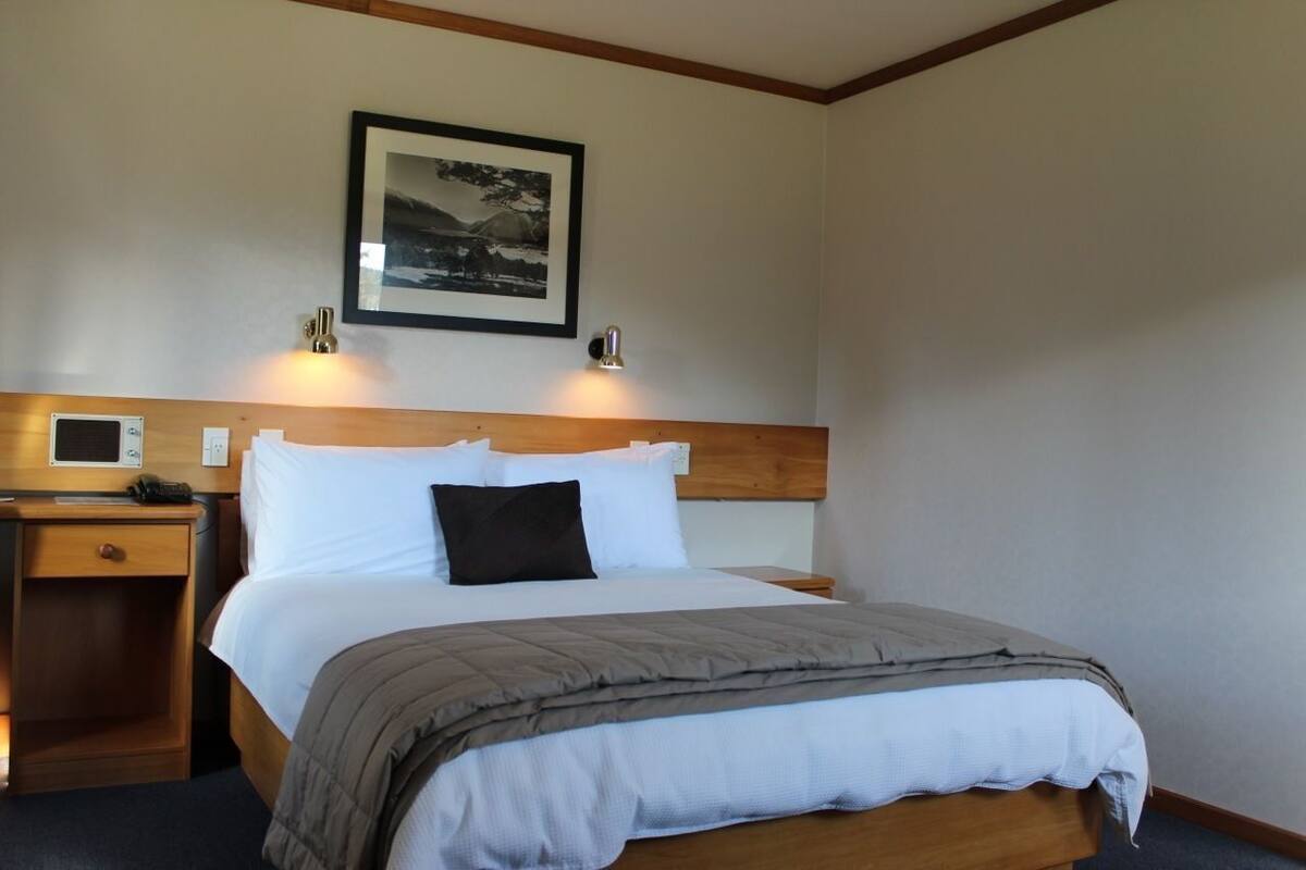 A hotel room with a bed, bedside table, lamp, and a framed picture on the wall.