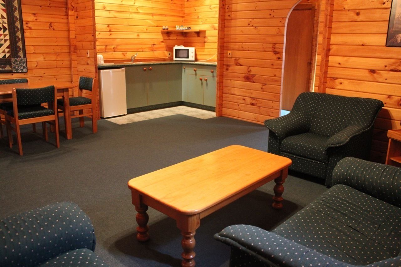 Un acogedor interior de cabaña con una mesa de comedor de madera, dos sillas, un sofá y una zona de kitchenette con microondas.