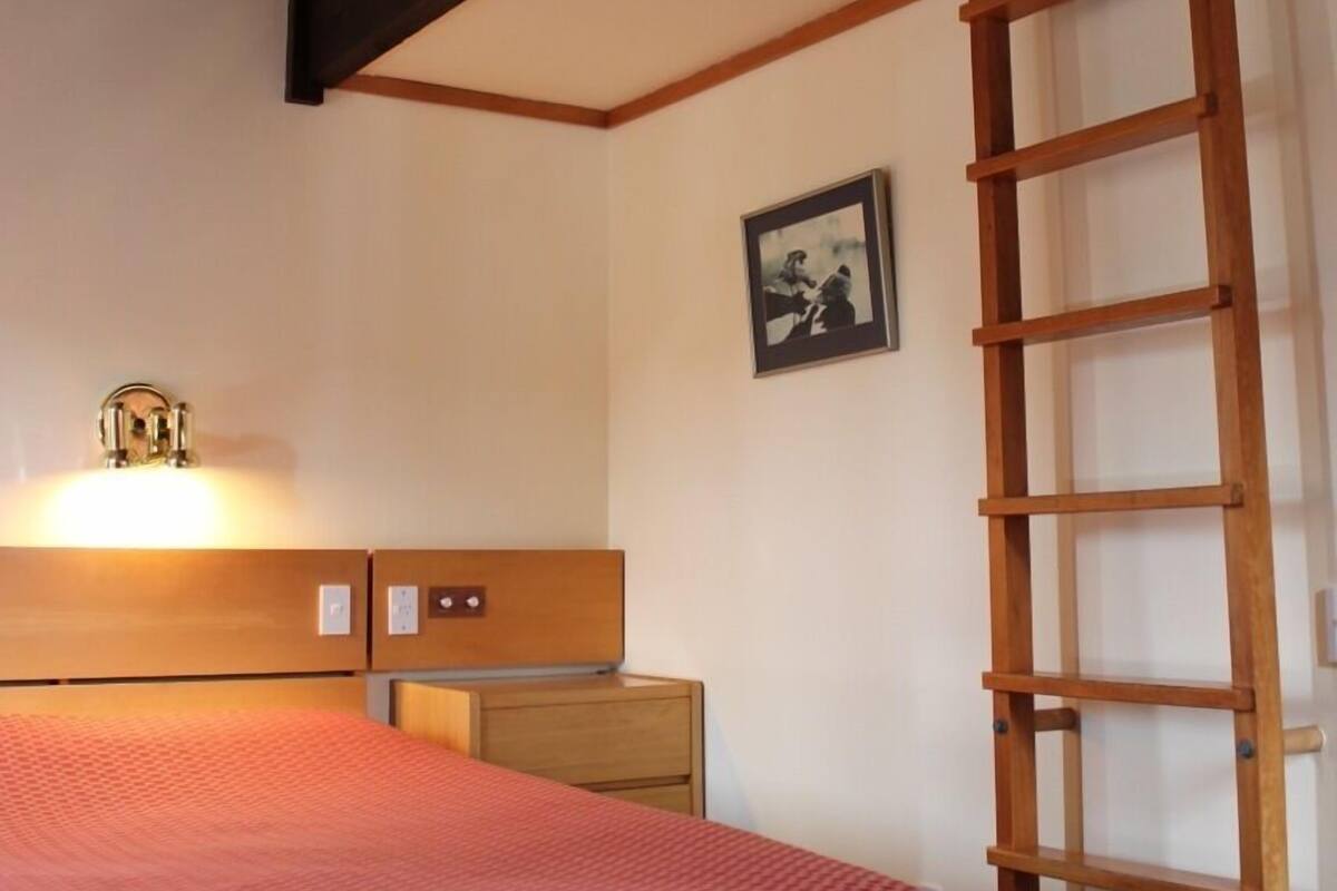 A bedroom with a bed, wooden ladder, nightstand, and a framed picture on the wall.