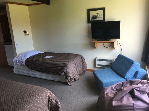 A hotel room with a bed, a TV on a stand, a small desk, and a chair.