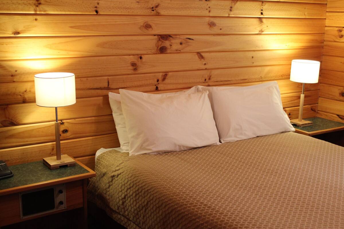 A wooden cabin-style room with two bedside tables, each with a lamp and a phone.