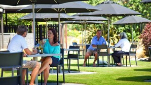 An outdoor patio with tables and chairs under umbrellas, surrounded by greenery. - Distinction Heritage Gateway Hotel (Omarama)
