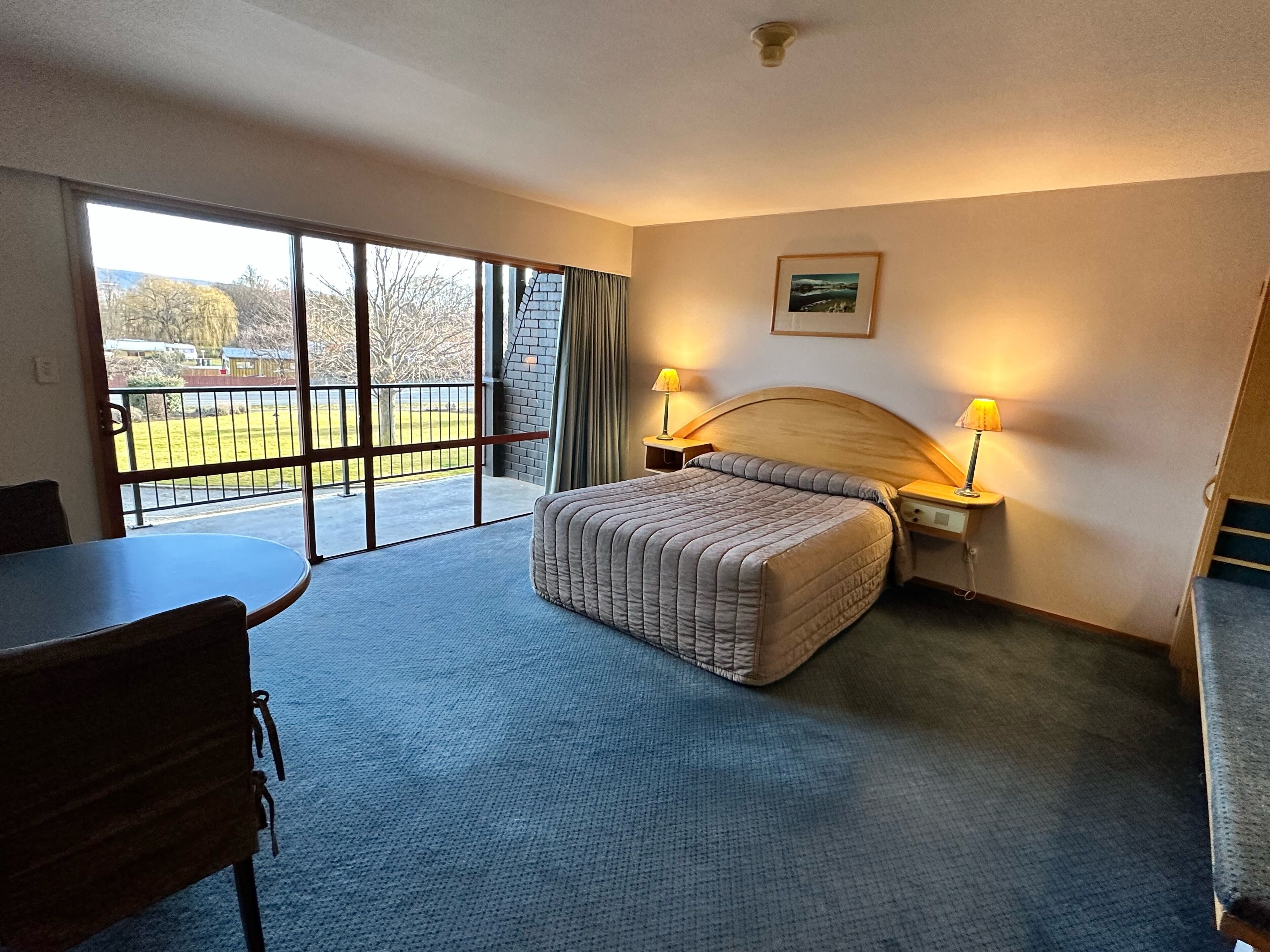 Une chambre d’hôtel avec un lit, deux lampes de chevet, une table et une chaise.