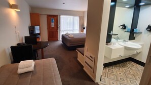 A hotel room with a bed, a desk, a TV, a bathroom with a sink and mirror, and a door leading to another room. - Distinction Heritage Gateway Hotel (Omarama)