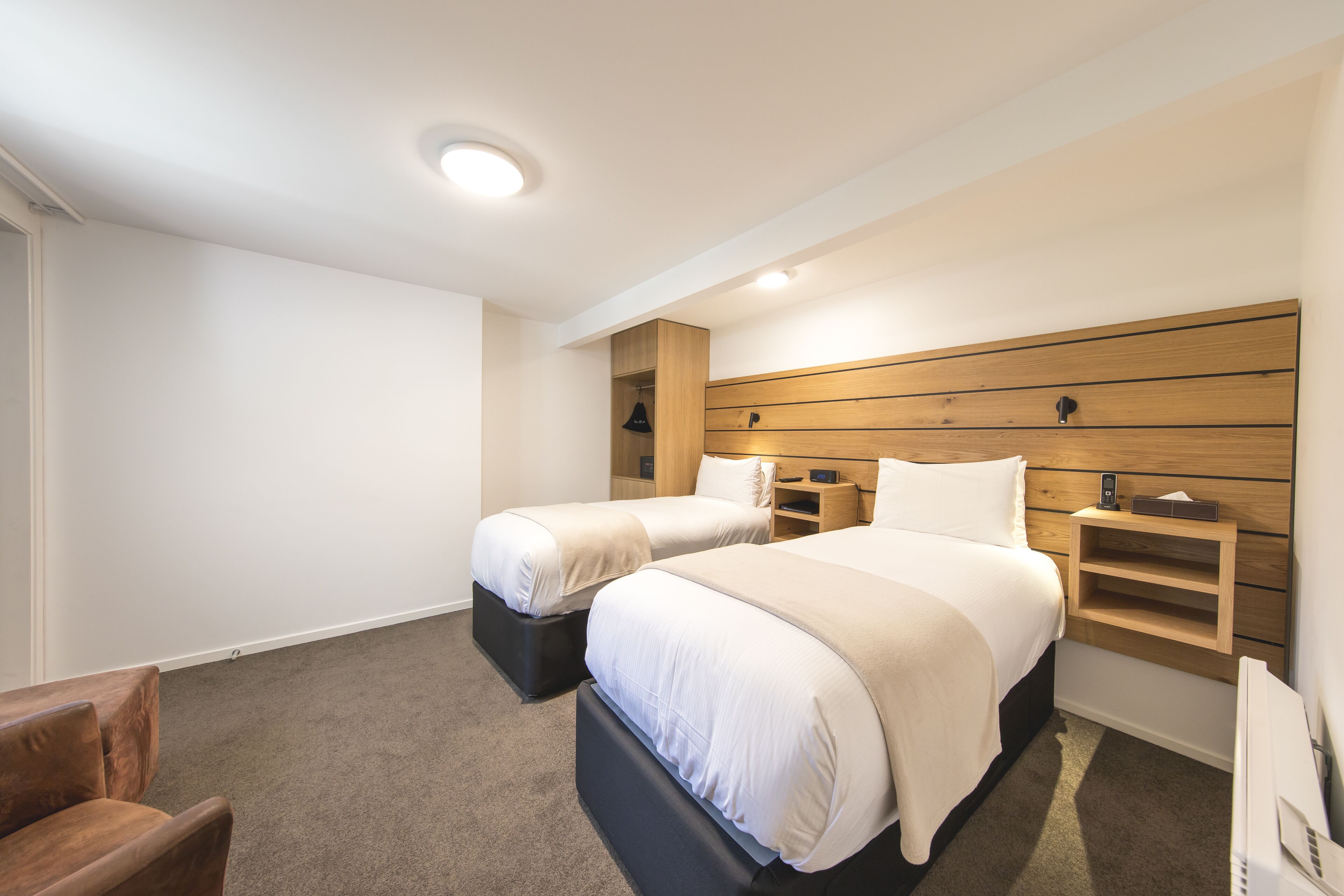 Une chambre d’hôtel avec deux lits, une tête de lit en bois, un petit bureau et une chaise.