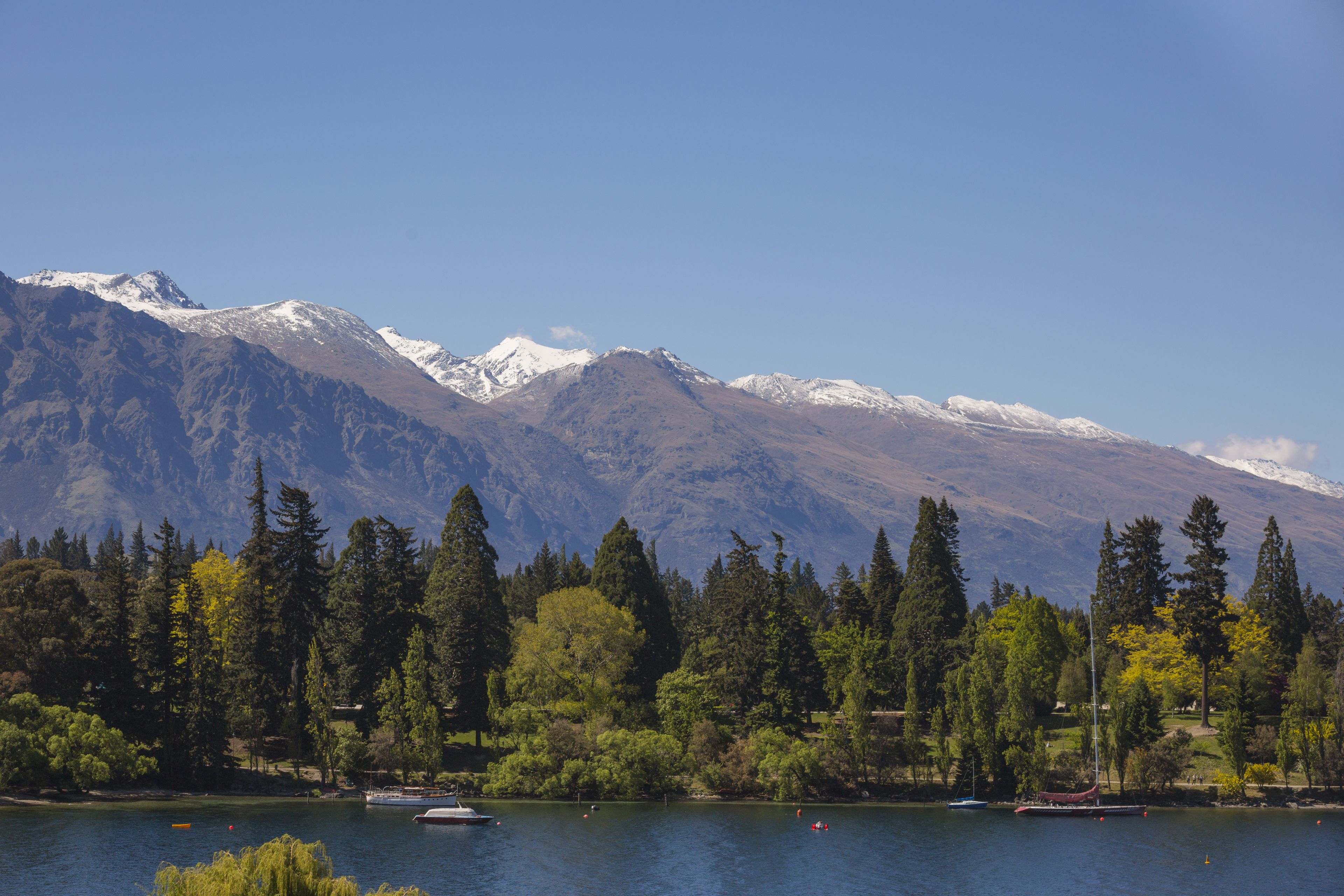 A lake with boats, surrounded by mountains and dense trees.
