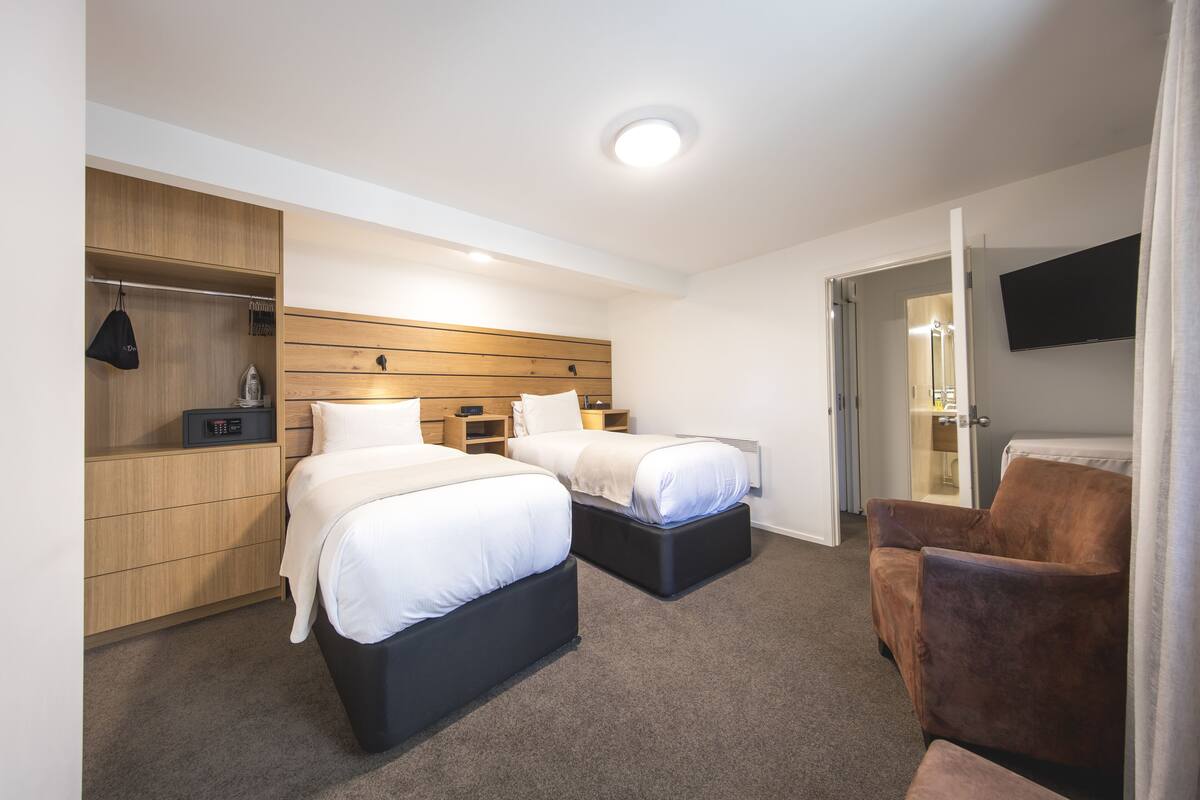 Ein Hotelzimmer mit zwei Betten, einem Kleiderschrank, einem Fernseher und einer Sitzecke.