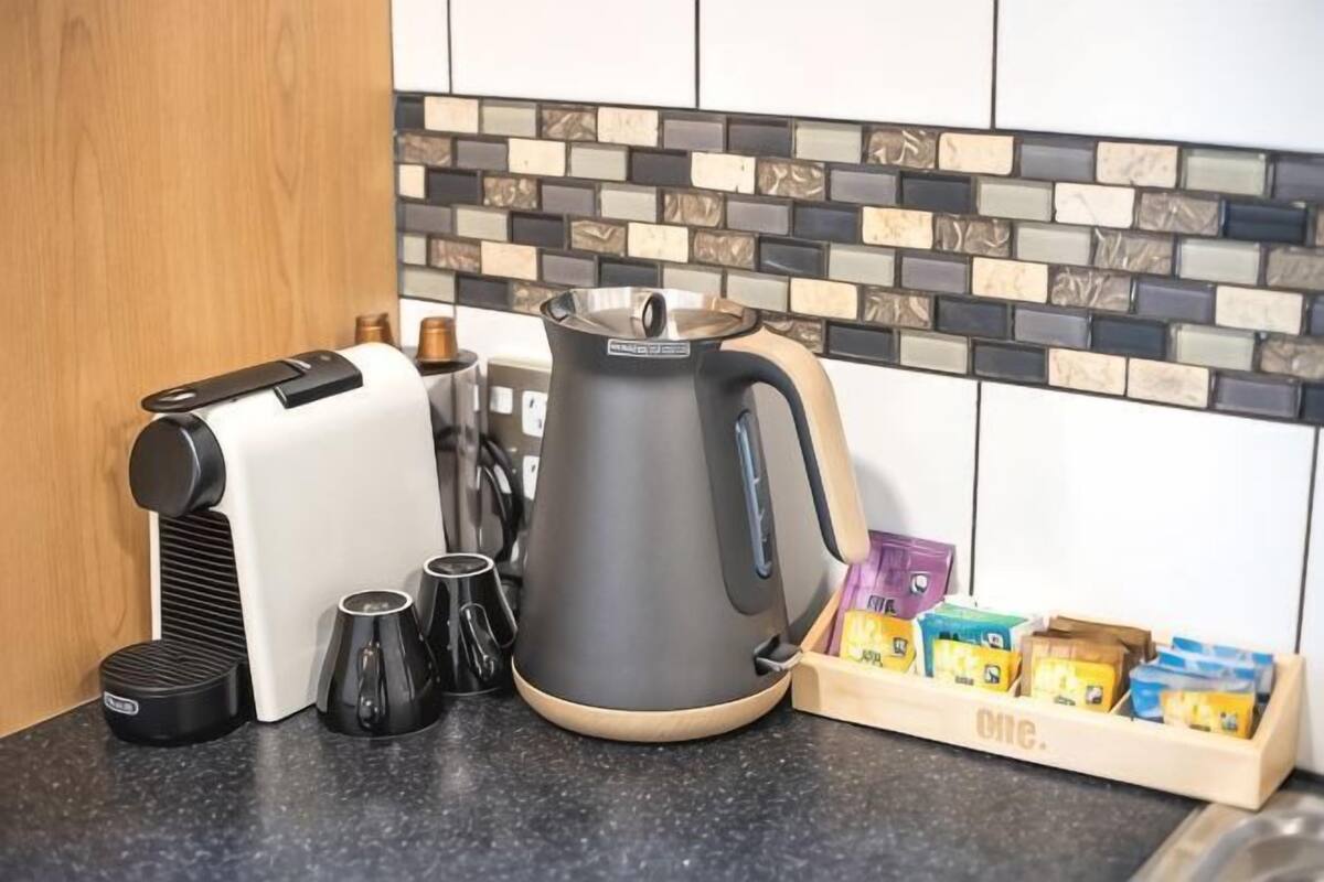 Eine Küche mit Kaffeemaschine, Wasserkocher und Kaffeekapseln auf der Arbeitsfläche.