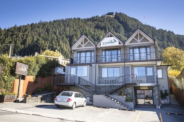 A two-story building with a reception area, a car parked in front, and a mountainous backdrop.
