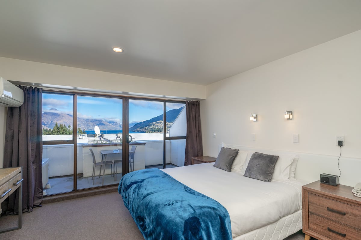 A bedroom with a large bed, a desk, and a view of mountains through a sliding door.