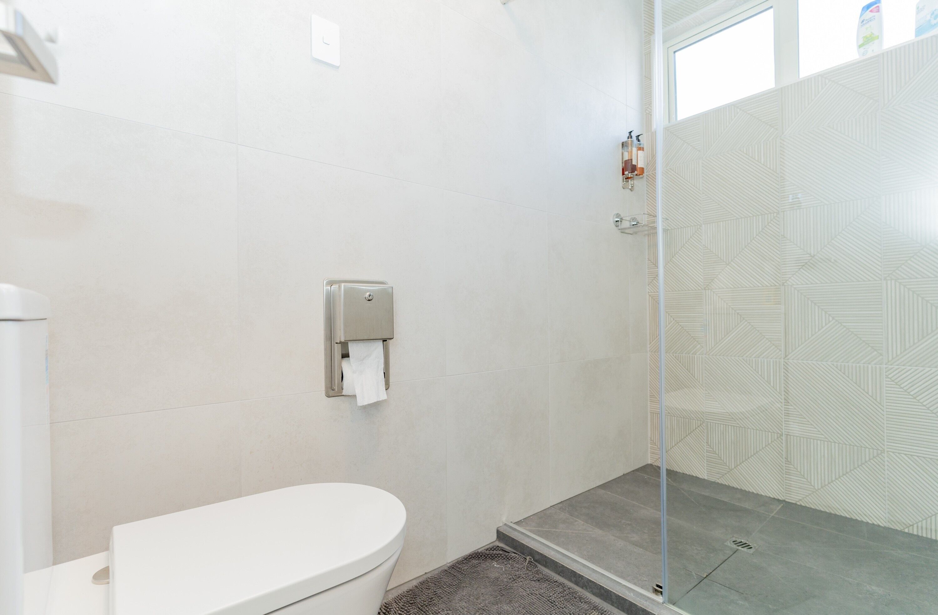 A modern bathroom with a toilet, a hand dryer, and a glass-enclosed shower area.