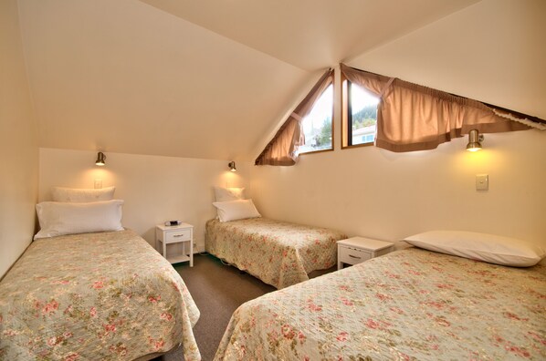 A bedroom with two single beds, each with a nightstand and lamp, and a window with curtains.