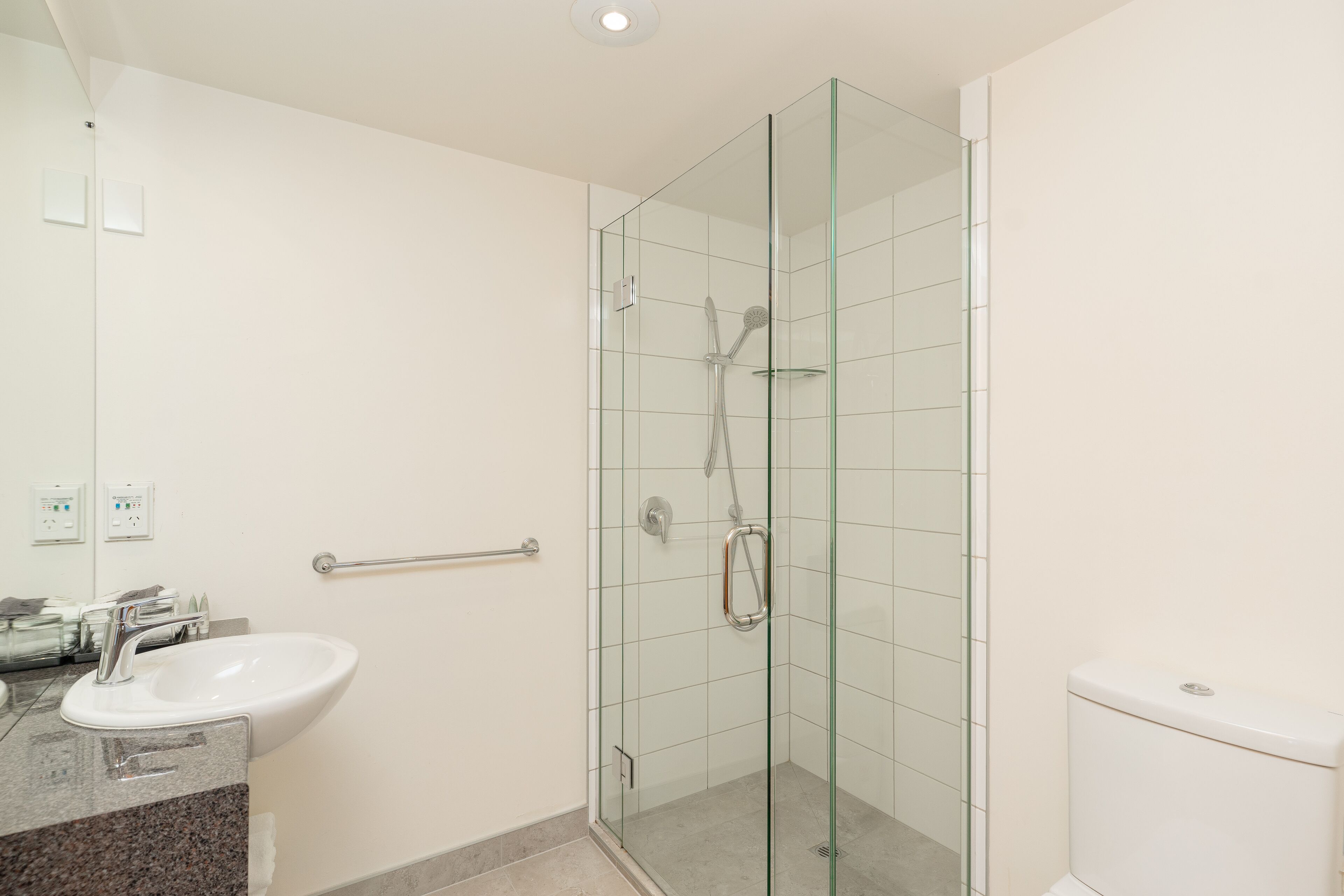 A bathroom with a glass-enclosed shower, a sink, and a toilet.