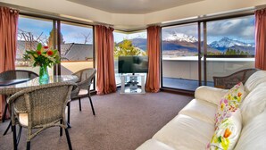 Un salon moderne comprenant un canapé, des fauteuils, une table à manger et un téléviseur. De grandes fenêtres offrent une vue sur les montagnes.