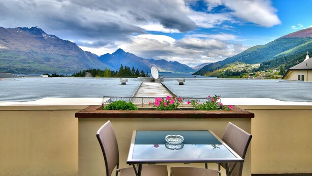 Une table avec deux chaises sur une terrasse sur le toit, offrant une vue sur les montagnes et un lac.