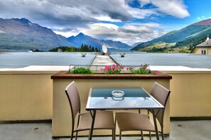 A table with two chairs on a rooftop terrace with a view of mountains and a lake.