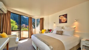 Une chambre spacieuse avec un grand lit, une chaise, une table de chevet et une vue sur un paysage montagneux, visible à travers une porte-fenêtre coulissante.