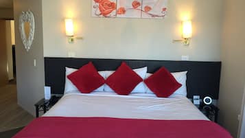 Una habitación de hotel con una cama grande, almohadas rojas y blancas, una manta roja y dos mesitas de noche con lámparas, además de una obra de arte en la pared sobre la cama.