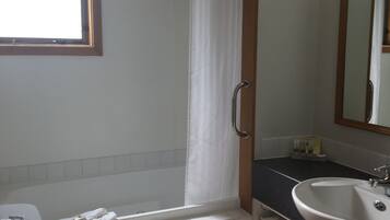 A bathroom with a toilet, sink, shower, and a window.