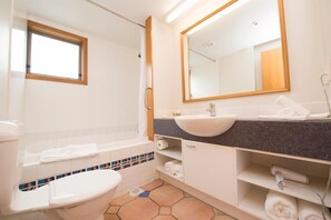 A modern bathroom with a white toilet, a sink with a dark countertop, a mirror, and a window. - Hurley's of Queenstown (Queenstown)