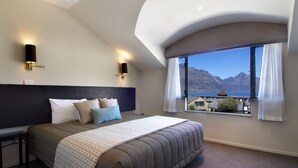 Una camera d'albergo moderna con un letto grande, due applique, vista sulle montagne e un soffitto curvo.