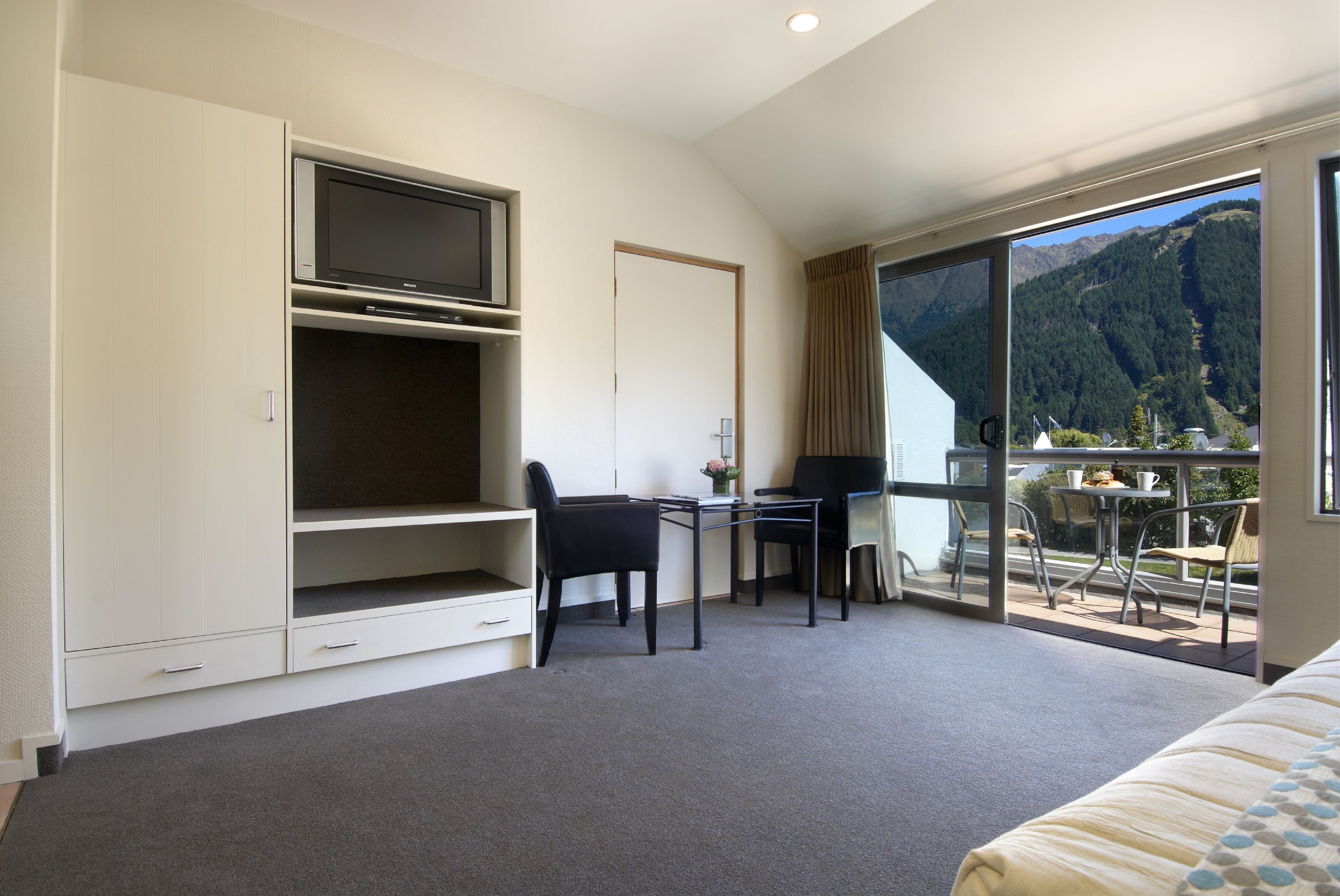 A room with a bed, a desk, a TV, and a balcony with a mountain view.