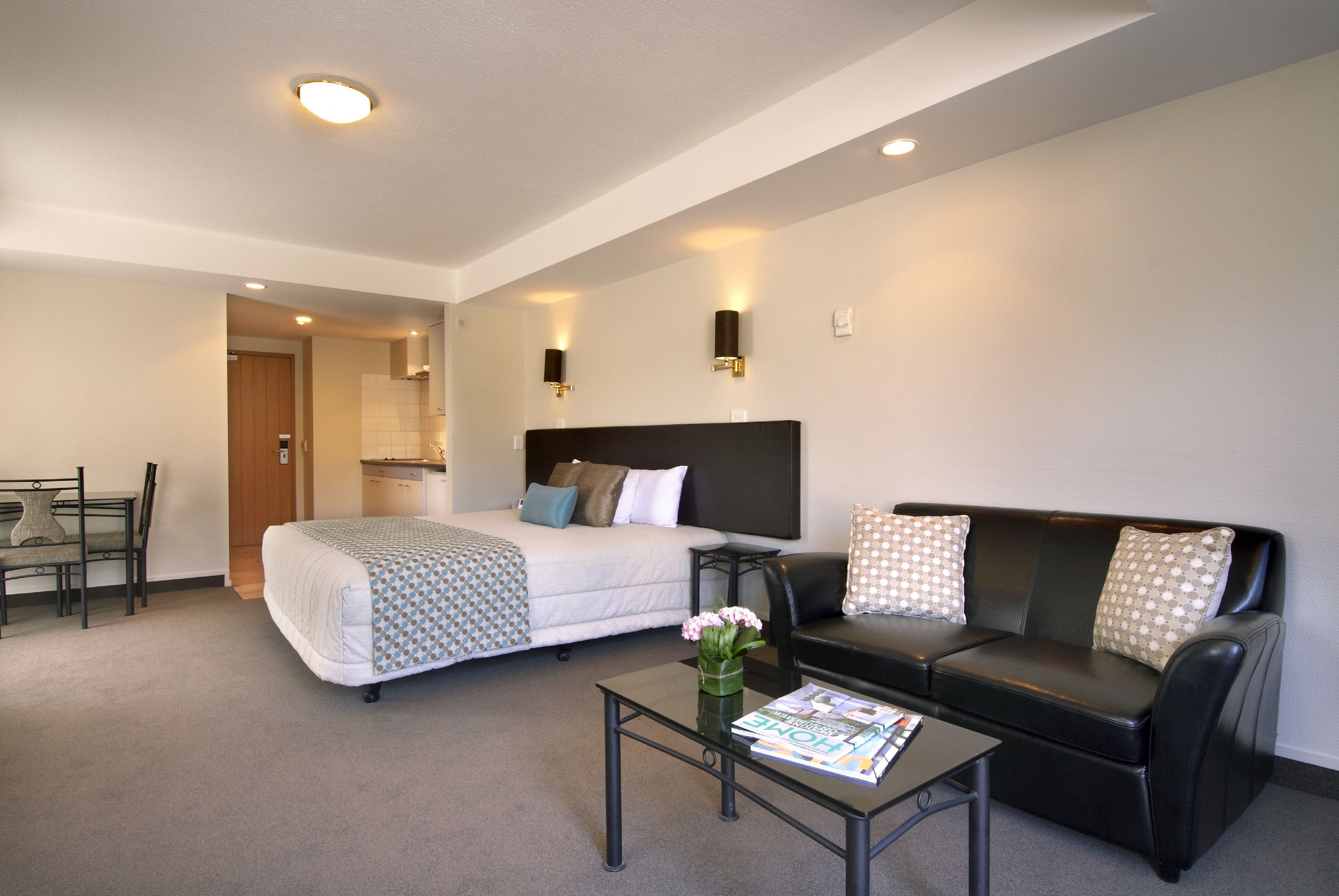 Una habitación de hotel moderna con una cama, un sofá de cuero negro, una mesa de centro de vidrio y un pequeño comedor.