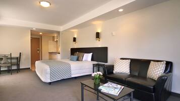 Una habitación de hotel moderna con una cama, un sofá de cuero negro, una mesa de centro de vidrio y un pequeño comedor.
