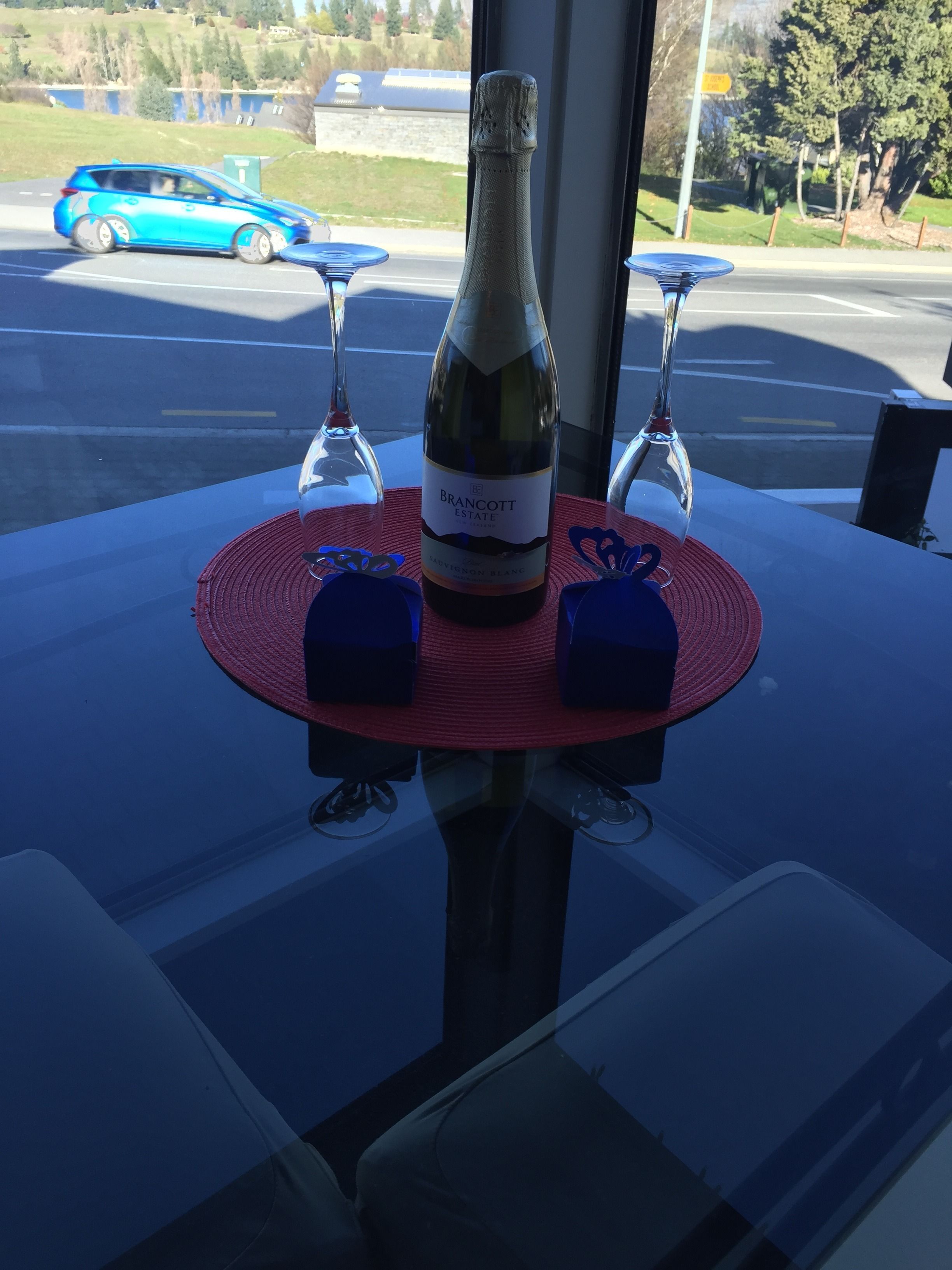 Une table avec une bouteille de vin Brancott Estate, deux verres et deux boîtes cadeaux bleues, le tout posé sur un set de table rouge.