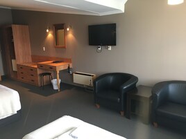 Una habitación de hotel moderna con un escritorio de madera, una silla de cuero negro, un televisor de pantalla plana grande y una cama.