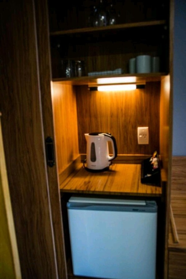 Una kitchenette compacta con un refrigerador pequeño, una tetera y un microondas.