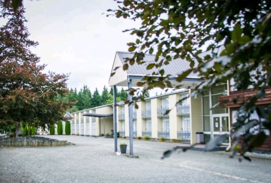 Un hôtel avec une série de chambres, un espace extérieur couvert et un parking.