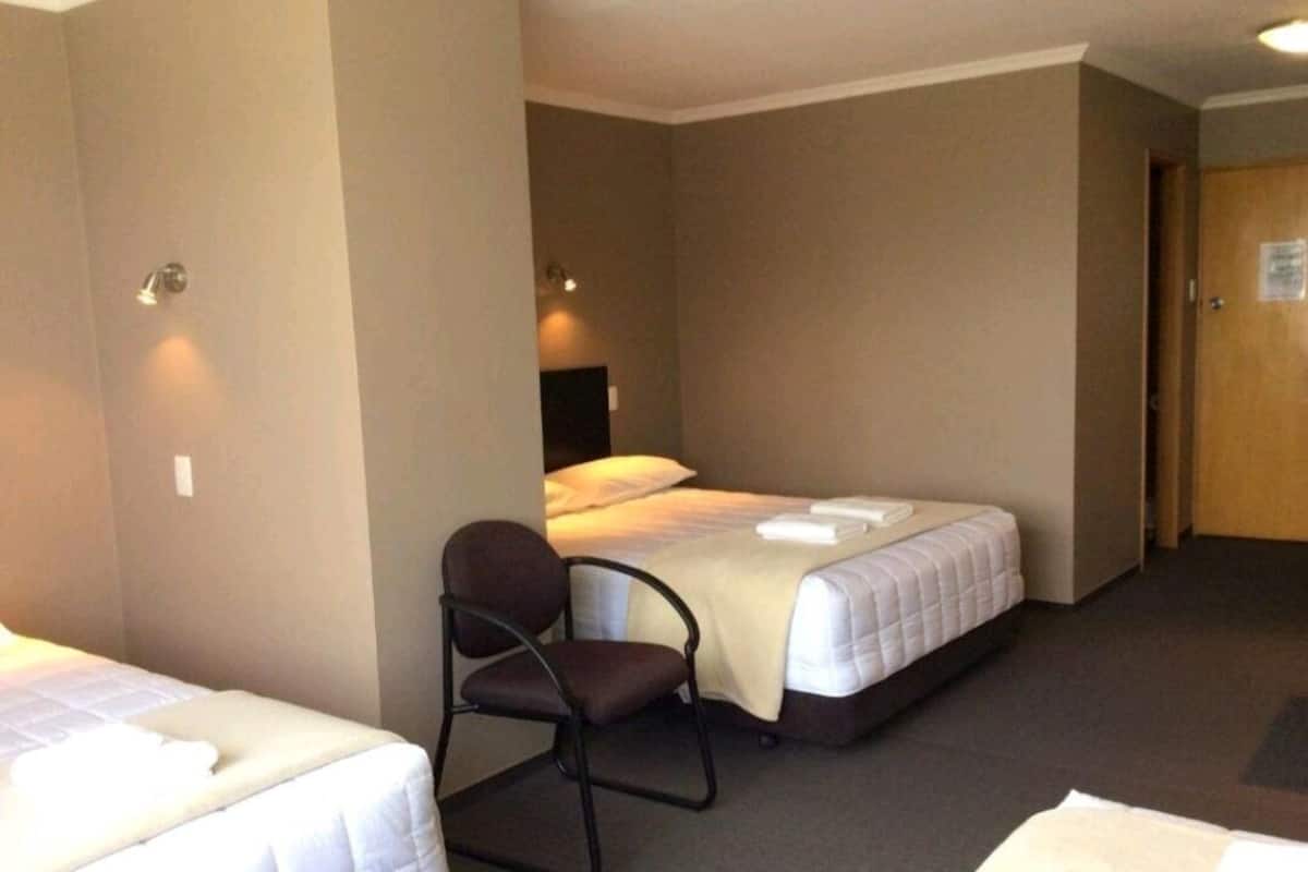 Habitación de hotel con dos camas individuales, una silla y una puerta.