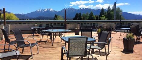 An outdoor patio with tables and chairs, overlooking a mountain range.