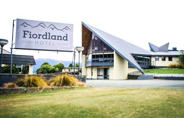 Un hotel llamado 'Fiordland' con un diseño arquitectónico moderno, que destaca por un cartel llamativo y una estructura de techo singular.