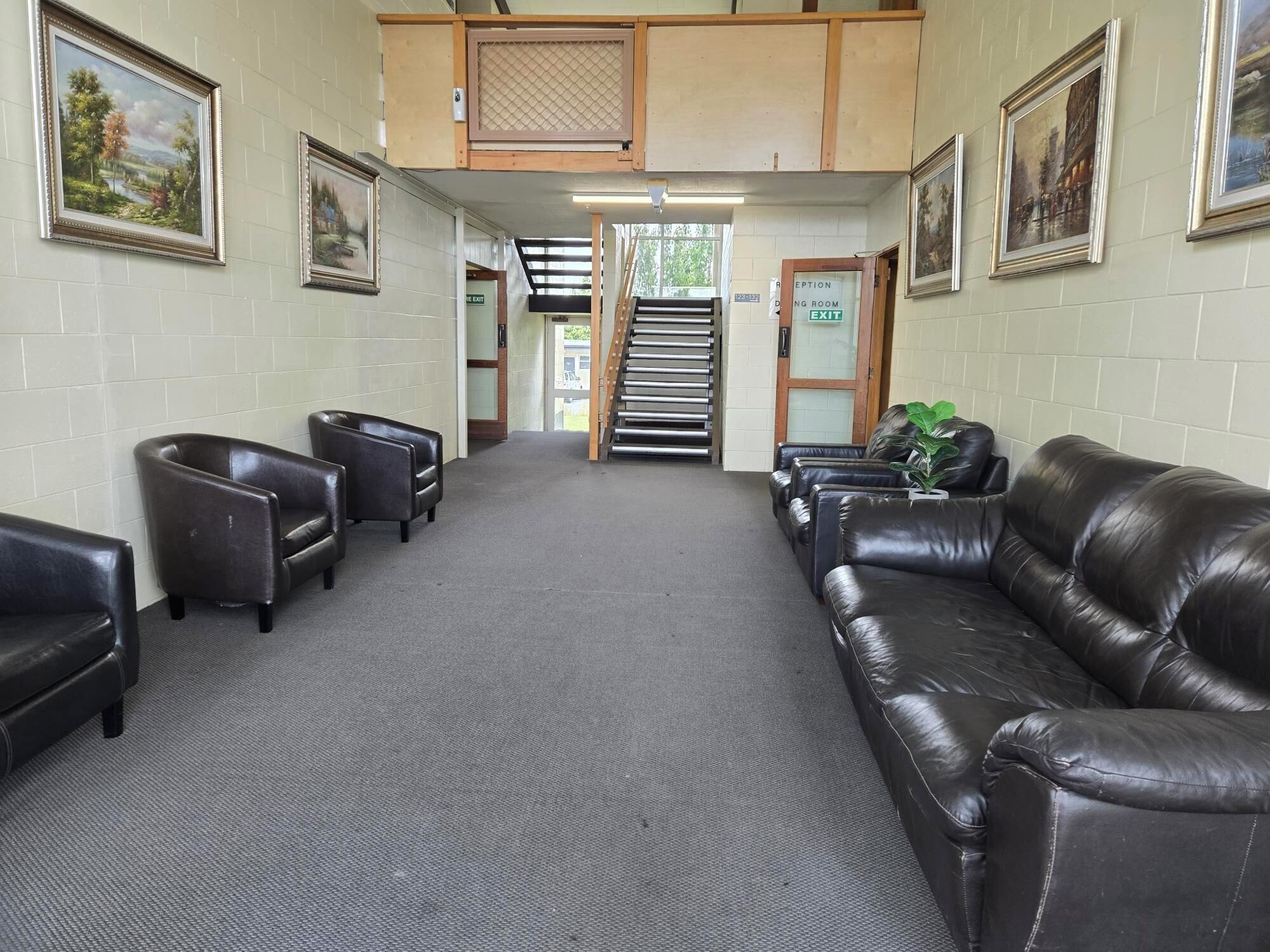 A reception area with leather sofas, framed landscape paintings, and a staircase leading to an upper level.