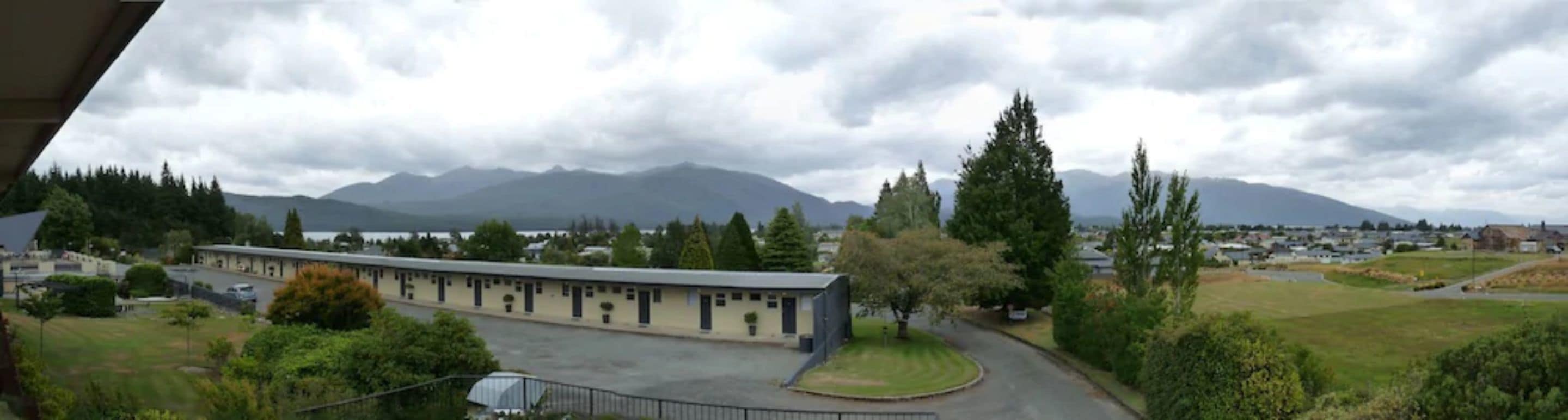 A long building with a flat roof, surrounded by greenery and a curved road.