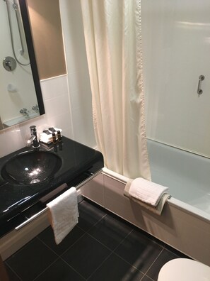 Un baño con lavamanos negro, un espejo, ducha con cortina y un inodoro.