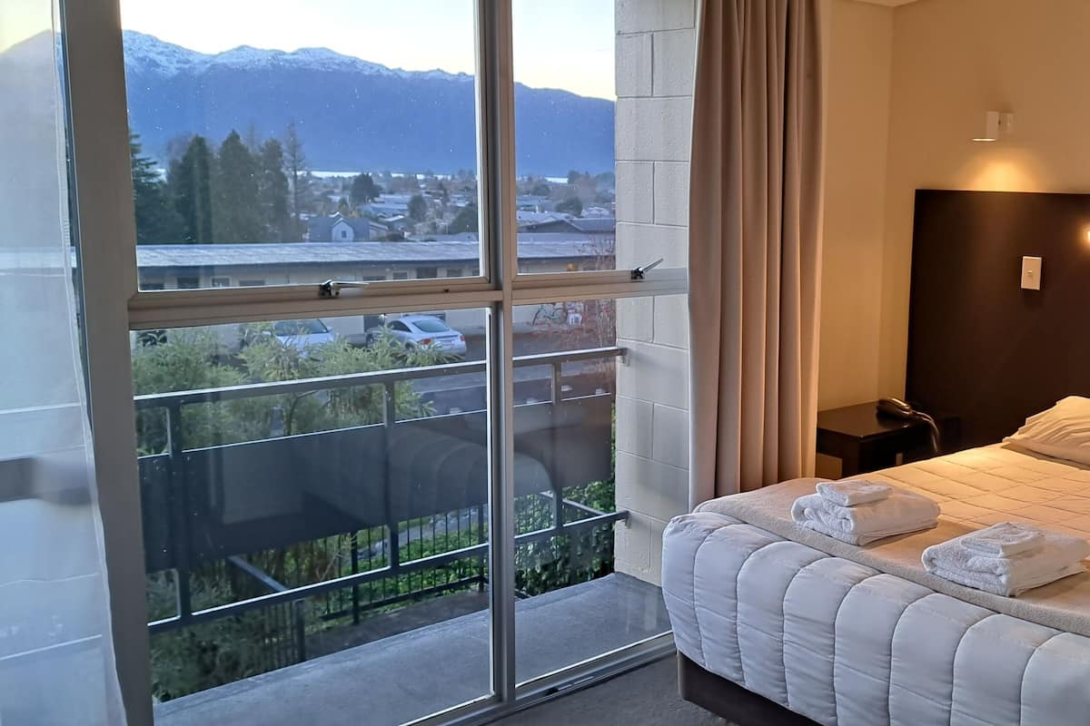 Una habitación de hotel con un ventanal grande, una cama con ropa blanca y una mesita de noche.