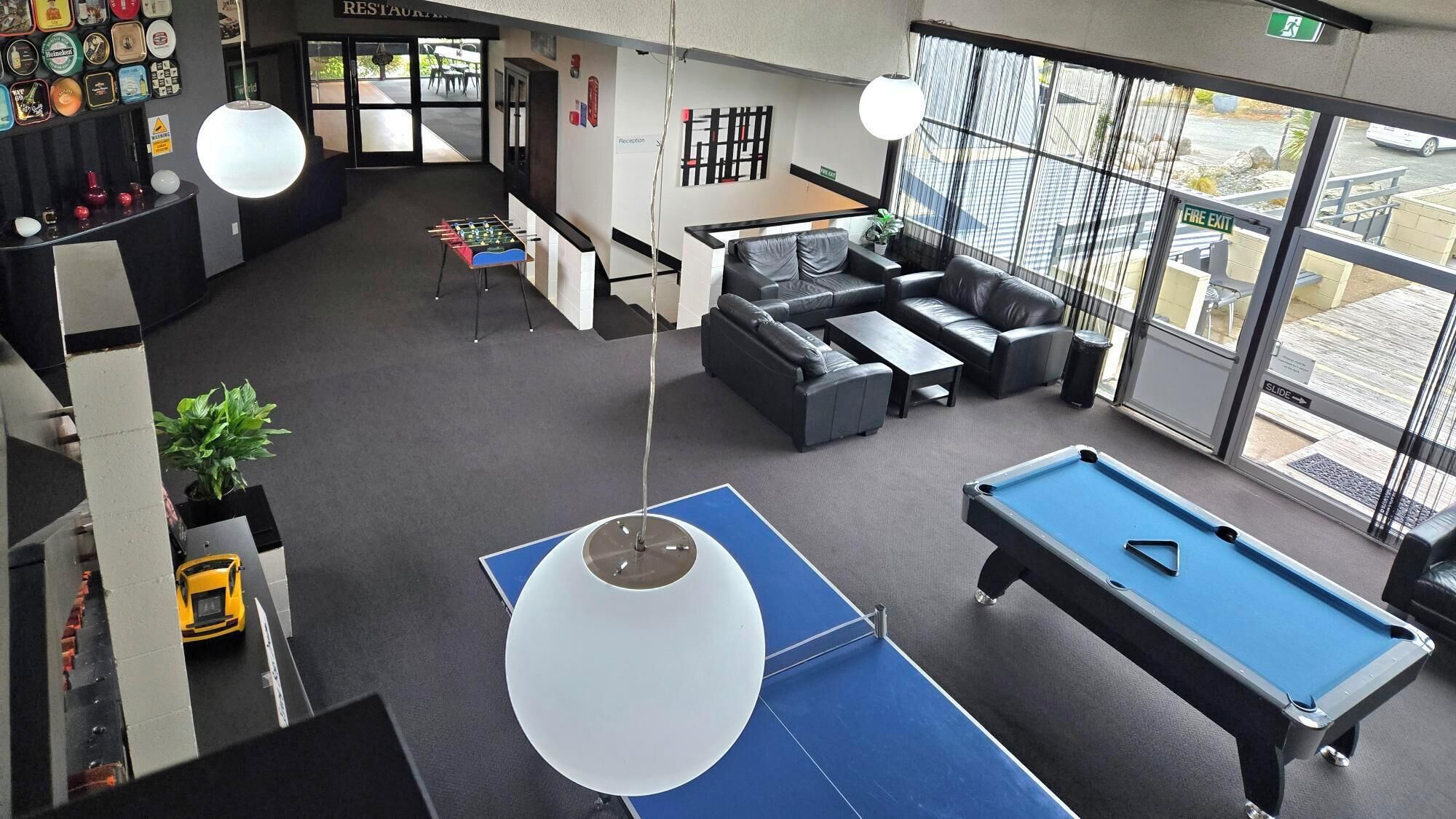 A modern indoor space with a pool table, a foosball table, a sofa, and a reception area.