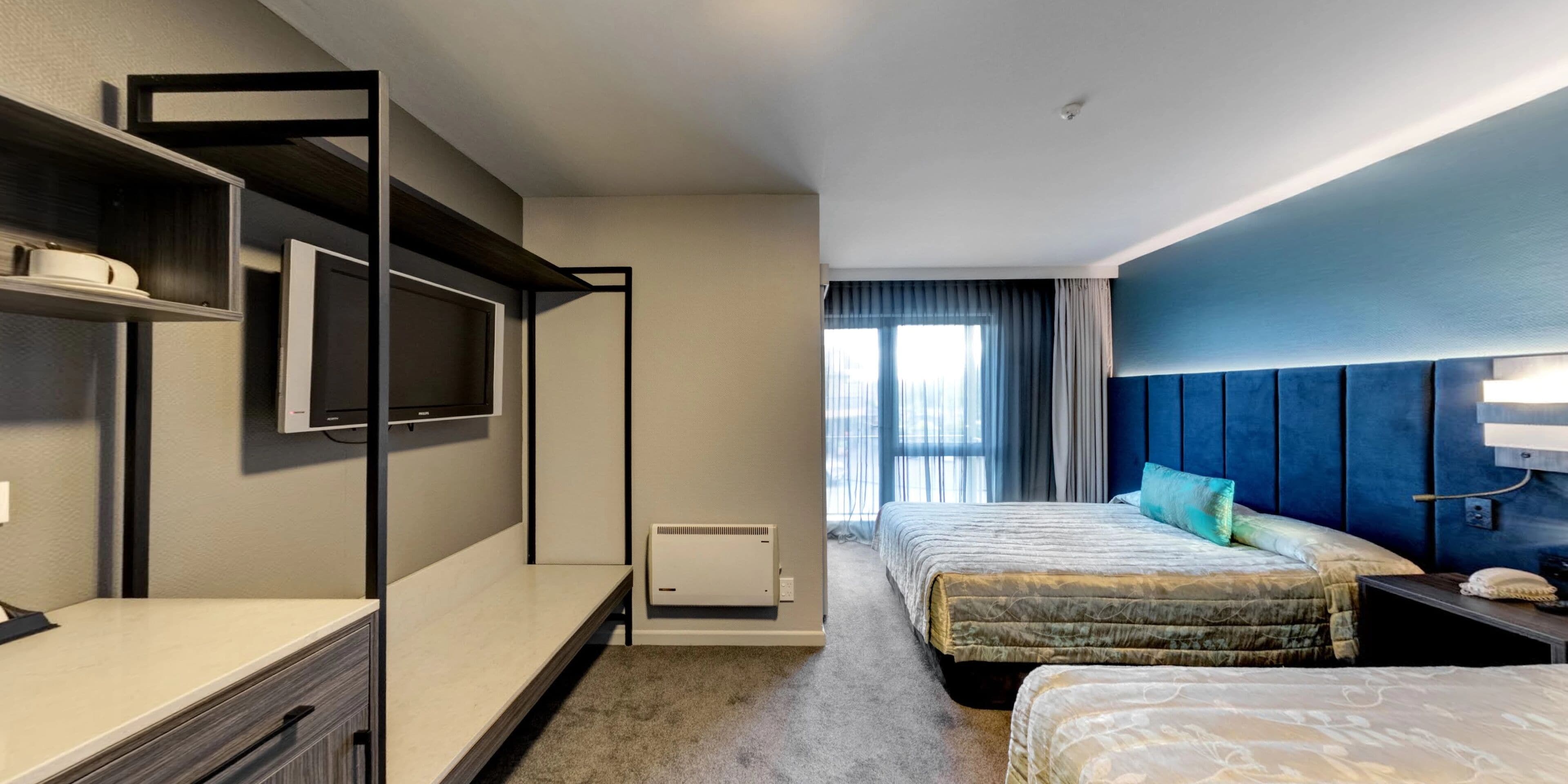 A hotel room with two beds, a TV, a desk, and a window with curtains.