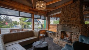 A cozy lounge area with a stone fireplace, leather seating, and large windows offering a view of the street. - Distinction Luxmore Hotel (Te Anau)