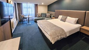 A hotel room with a large bed, a sofa, a small table, and a TV. - Distinction Luxmore Hotel (Te Anau)