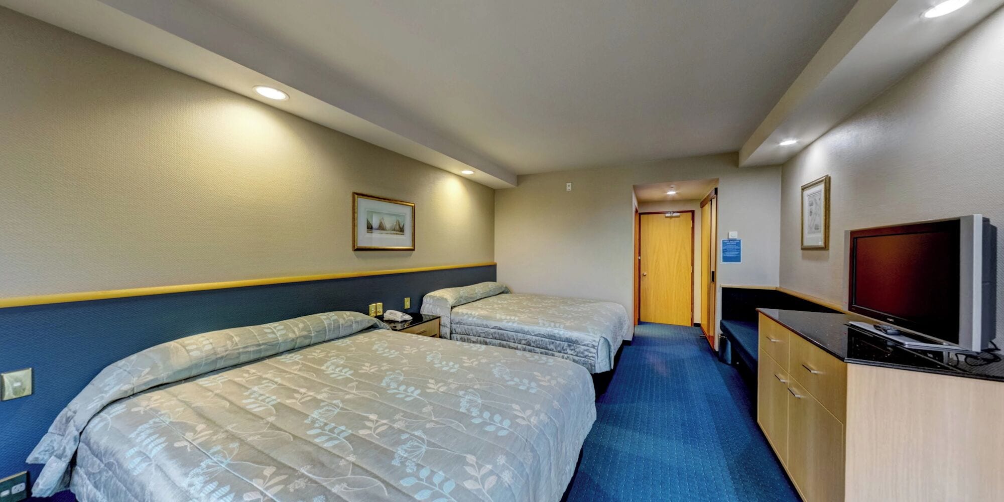 Habitación de hotel con dos camas, un escritorio con televisor y una puerta que da a otra habitación.