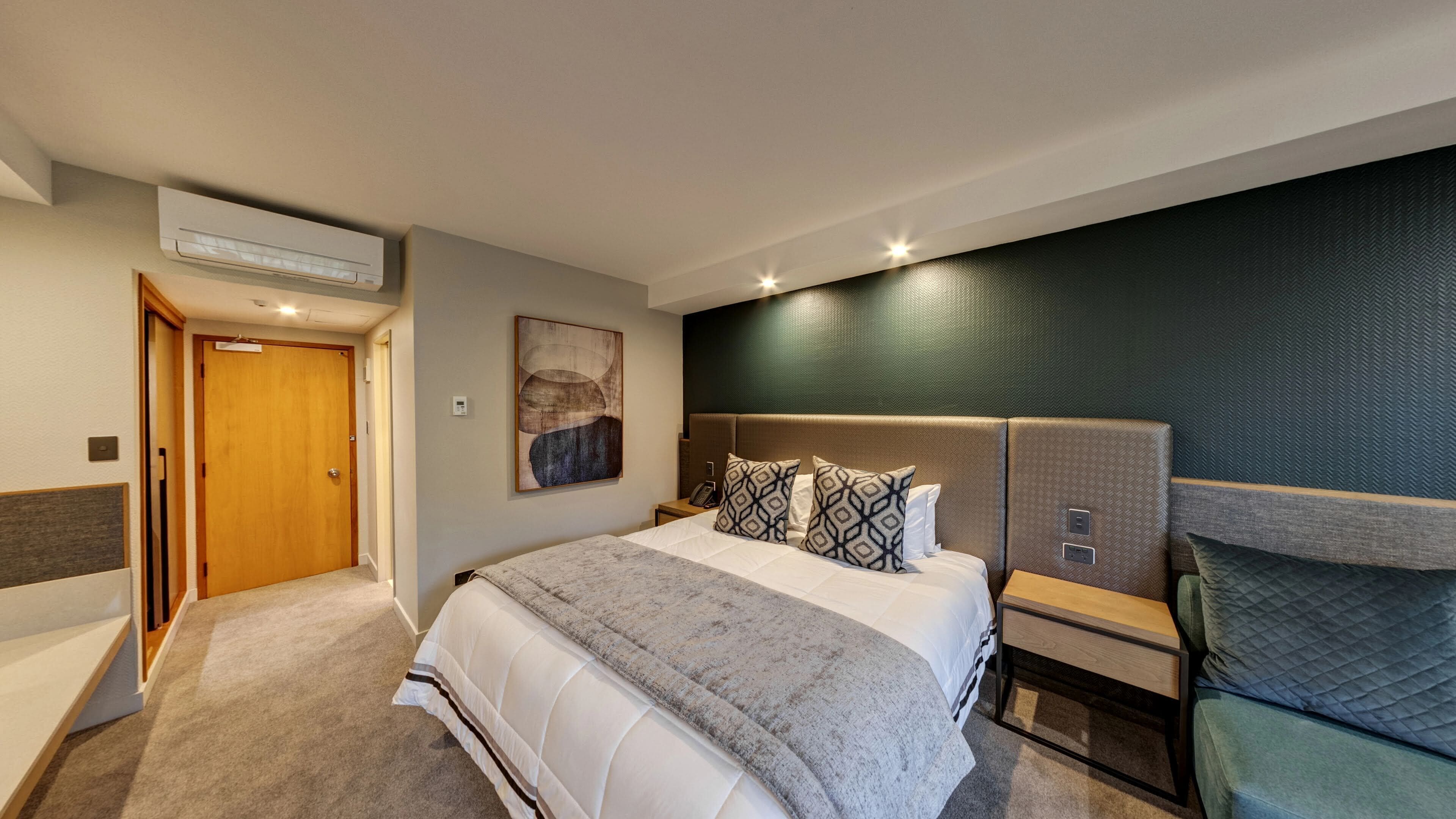 A hotel room with a bed, bedside table, and a wall-mounted air conditioner.