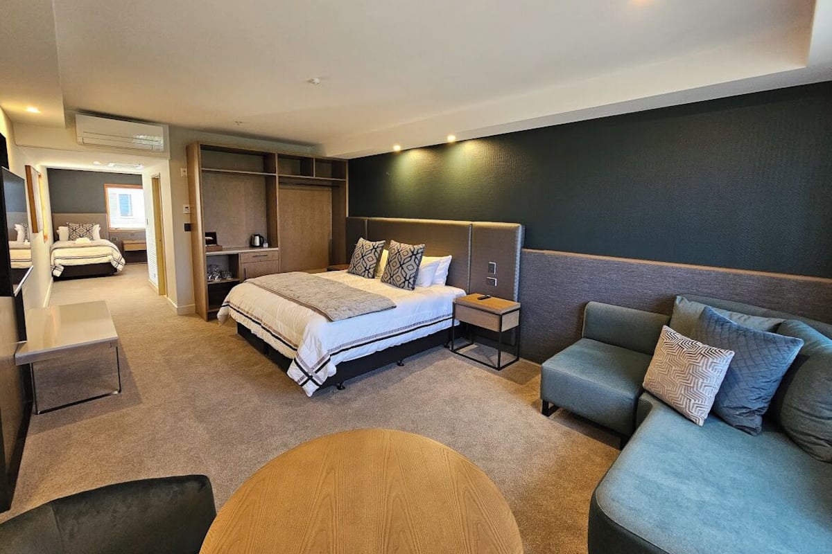 A modern hotel room with a large bed, a sofa, a desk, and a chair.