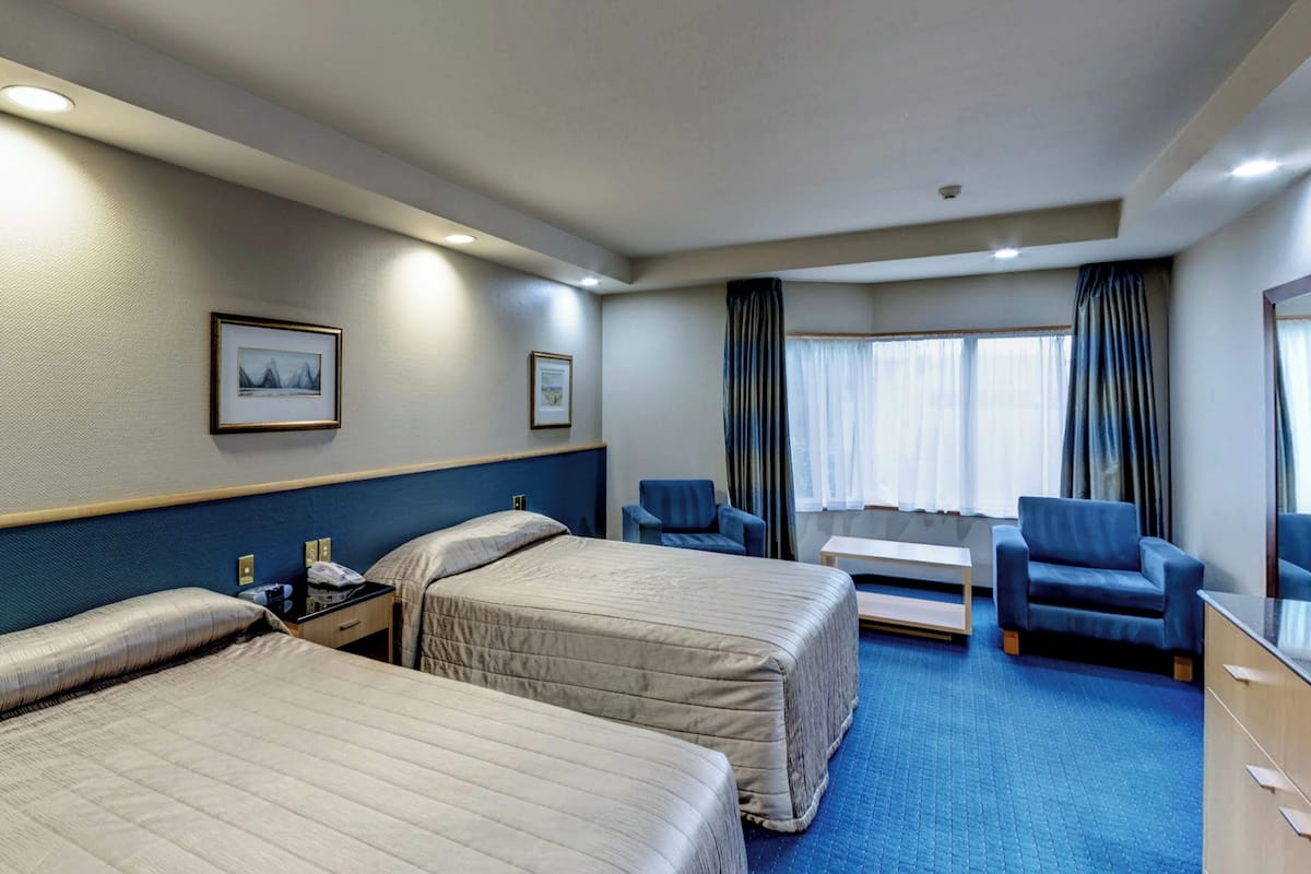 A hotel room with two beds, a desk, a chair, and a window with curtains.