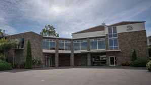 A modern building with a stone facade, large windows, and a prominent 'D' logo. - Distinction Luxmore Hotel (Te Anau)