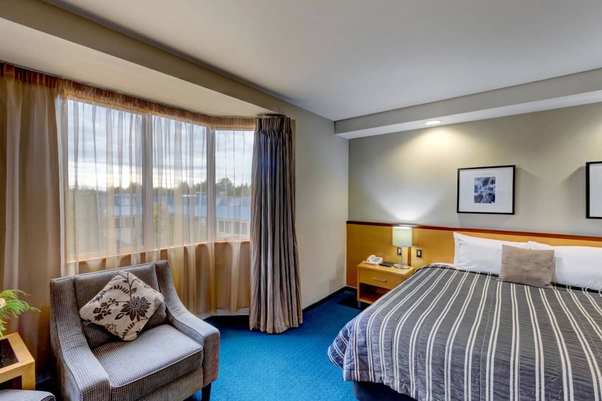 A hotel room with a bed, a chair, a nightstand, a lamp, and a window with curtains.